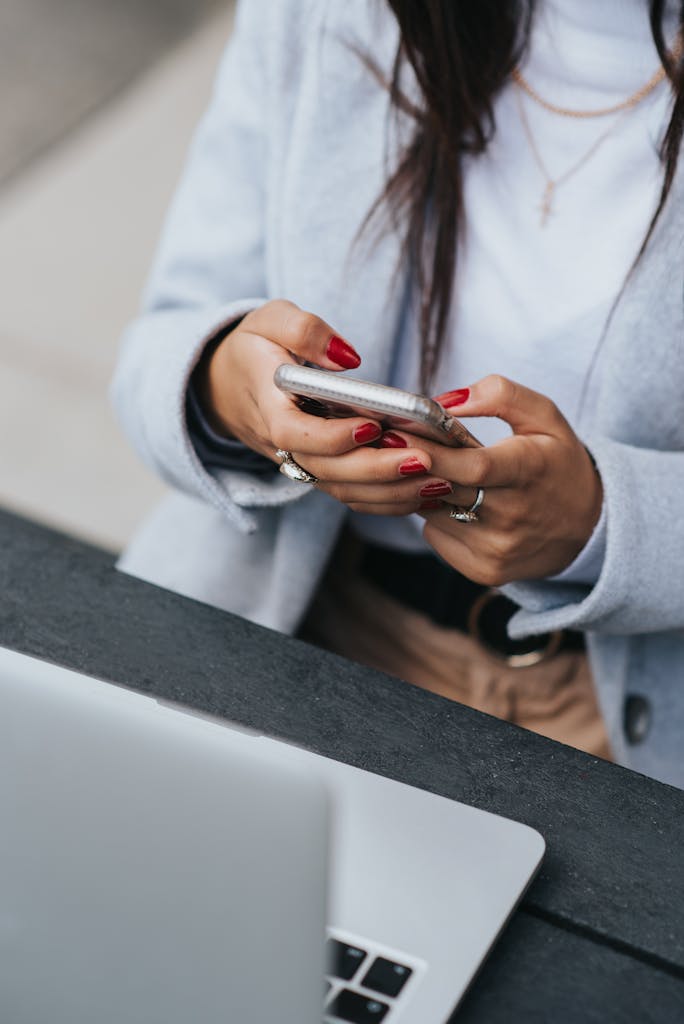 Crop ethnic businesswoman surfing internet on smartphone near laptop outdoors